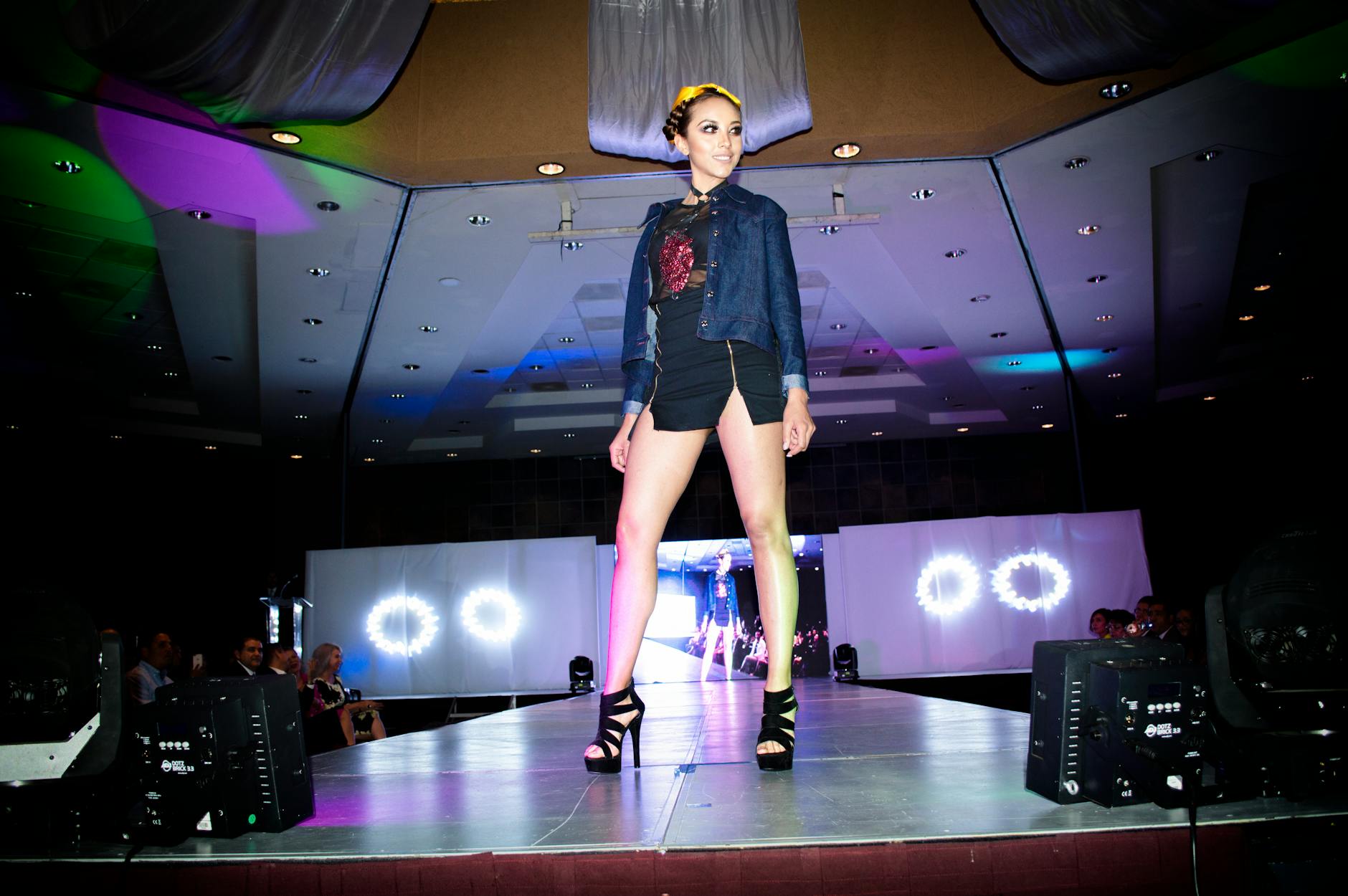 Fashion runway show with models walking and audience seated watching the presentation