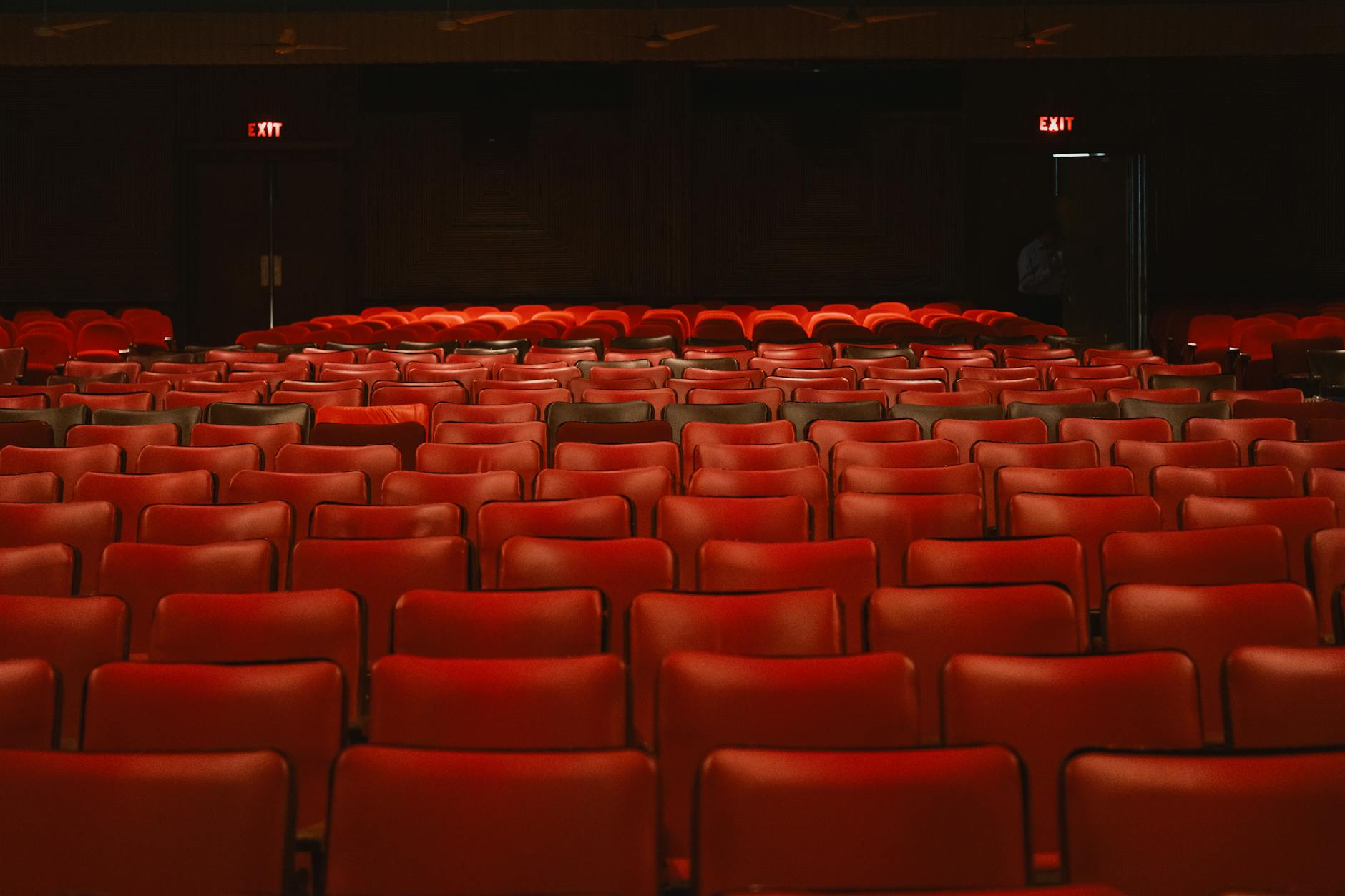 Empty movie theater with red seats facing illuminated screen