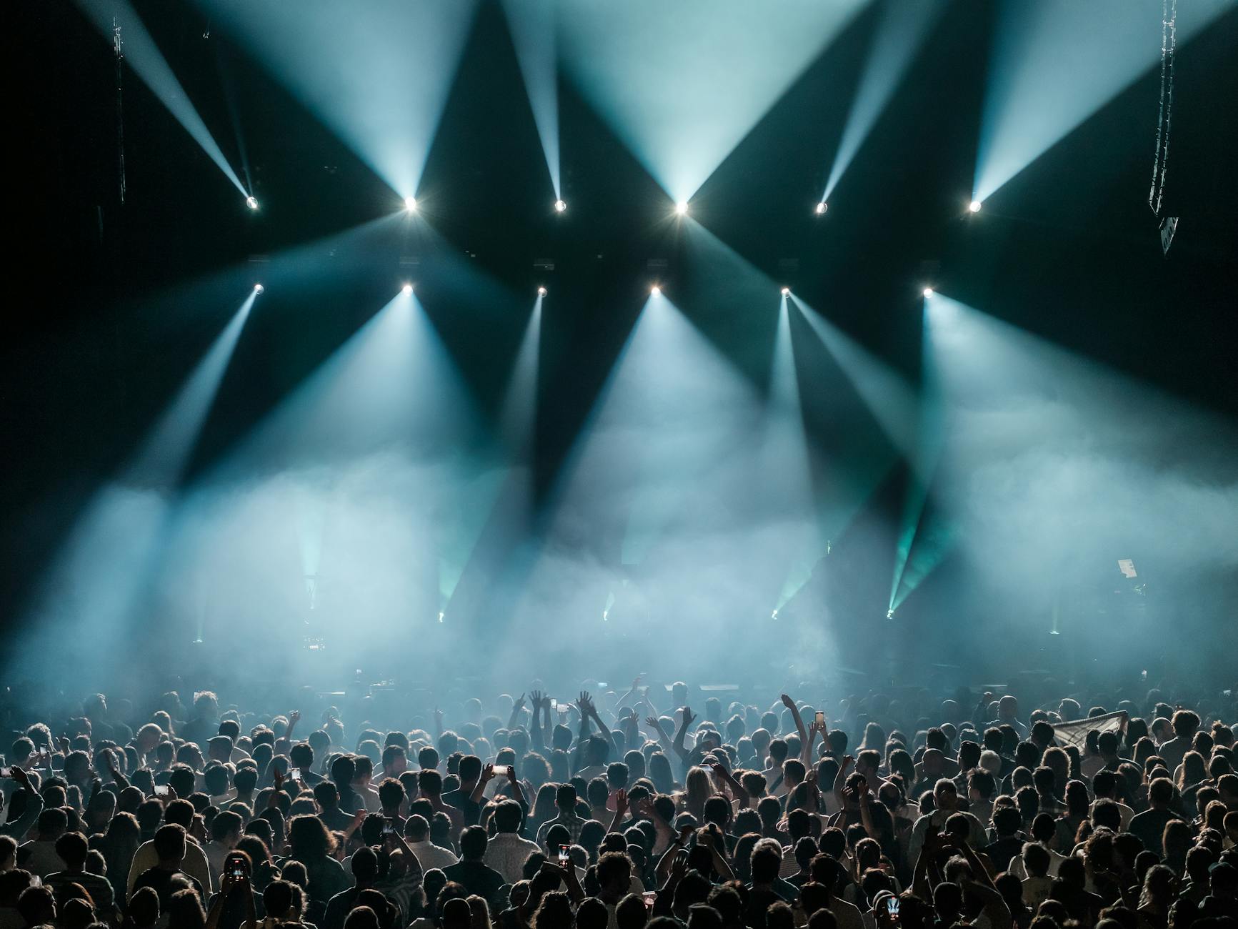 A large crowd at an indoor arena concert with colorful stage lighting