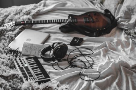 A young artist recording music in a home bedroom studio setup with a laptop and microphone