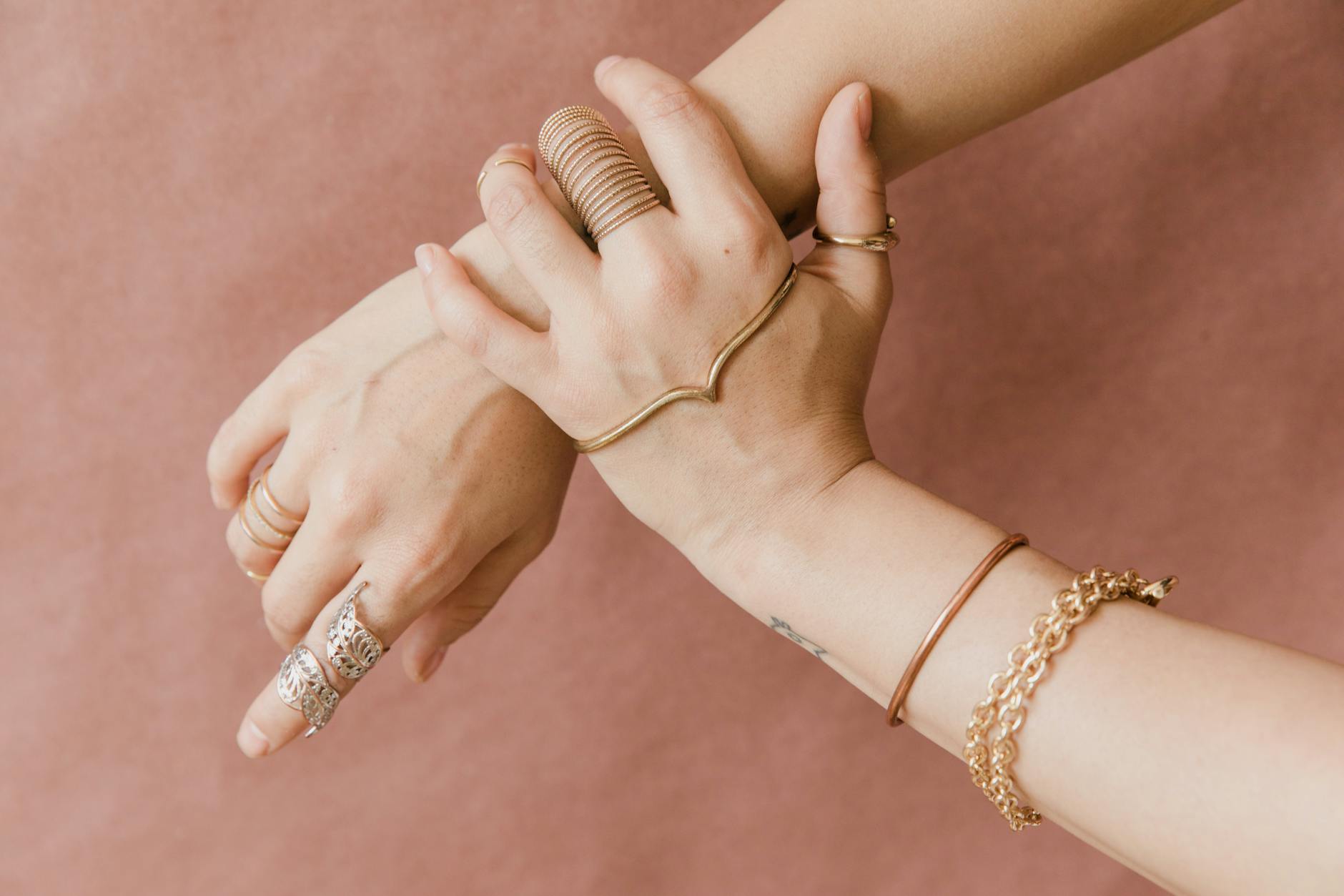 Stacked gold bracelets and rings displayed on a neutral surface