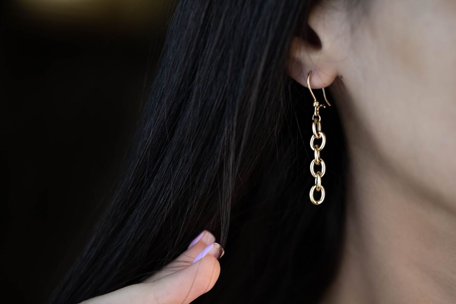 Close-up of elongated gold drop earrings against a neutral background