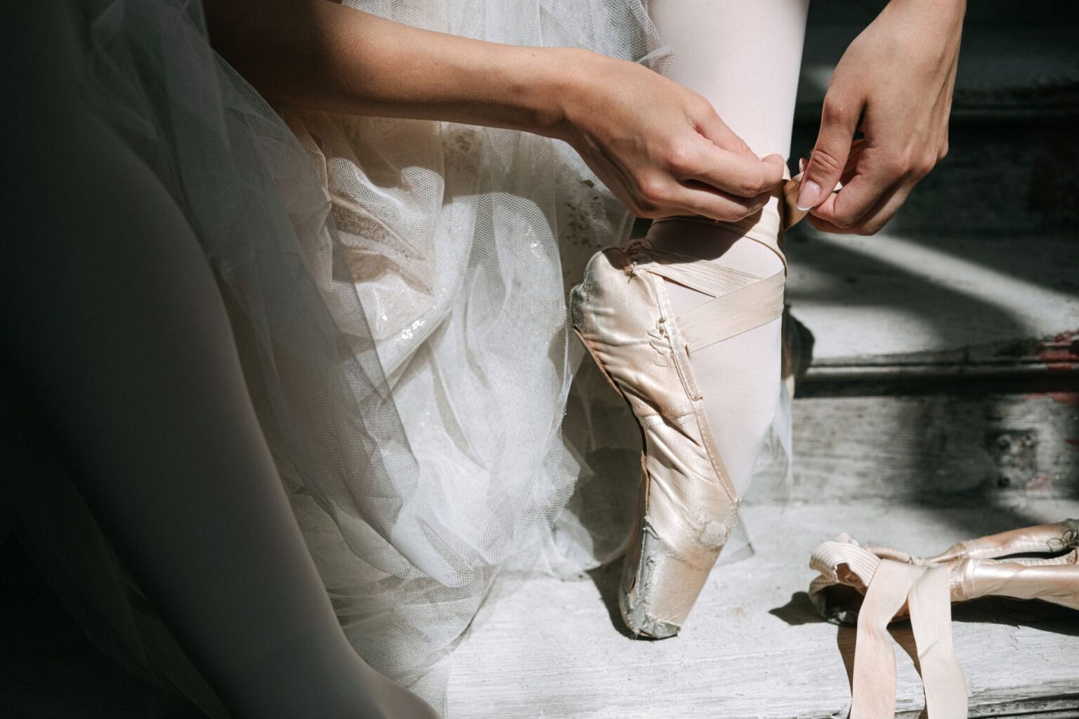Close-up of satin ballet pointe shoes with ribbon ties on a wooden floor