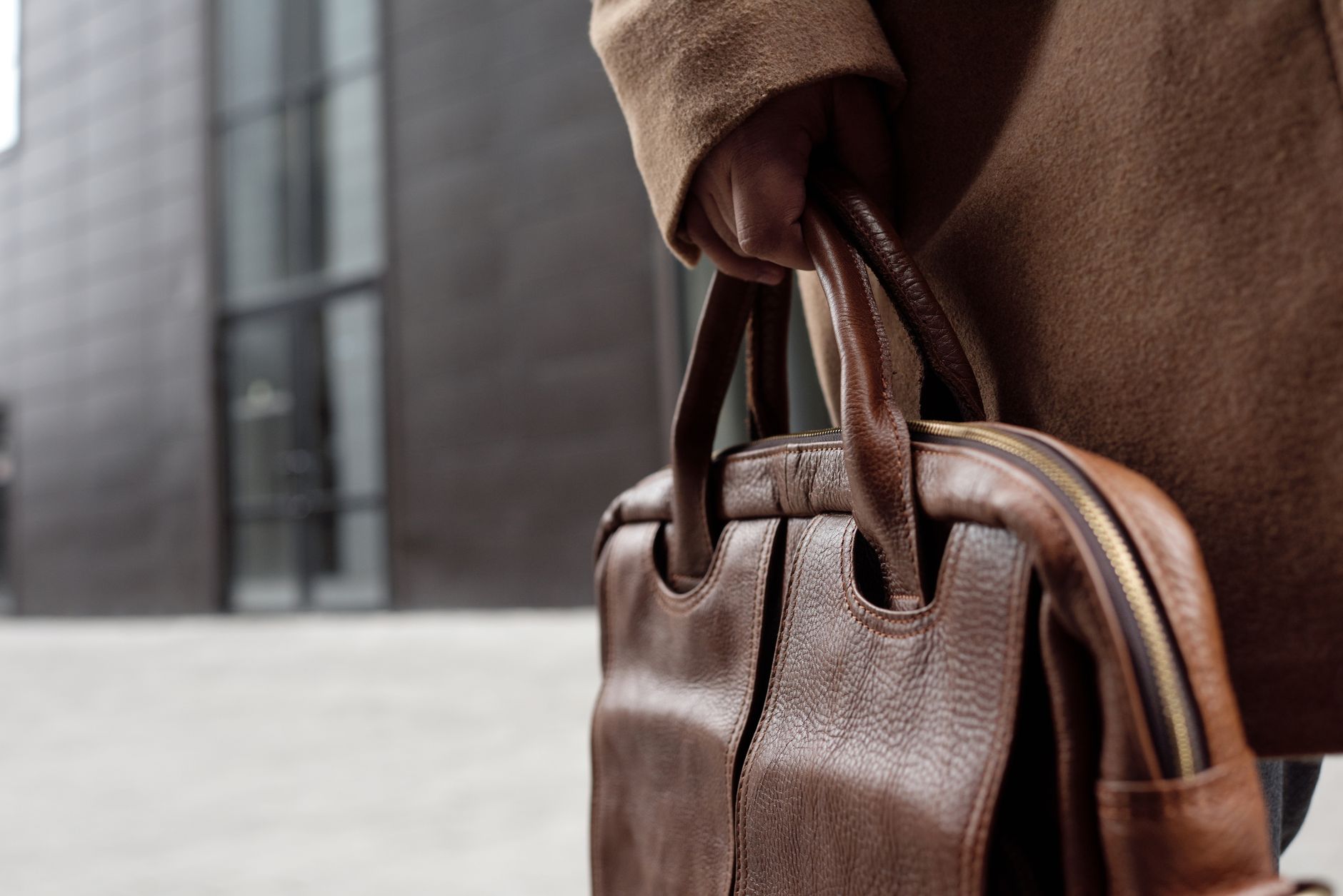 A woman in tailored clothing carrying a structured top-handle bag on her shoulder