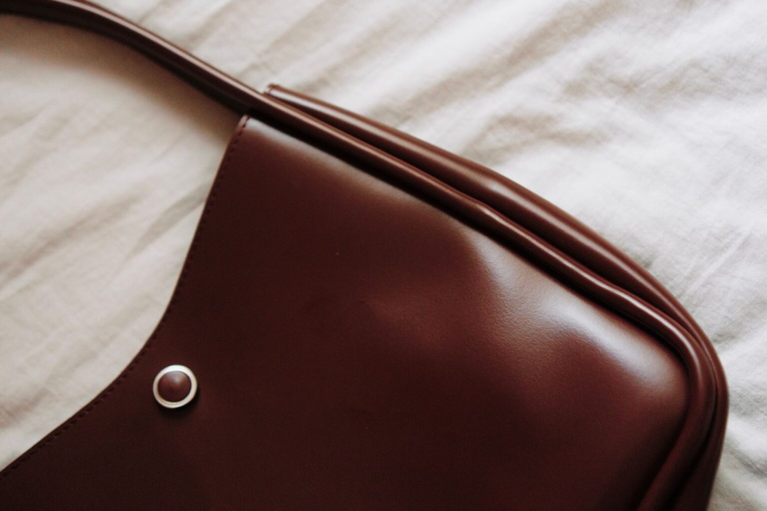 A structured leather shoulder bag resting on a neutral surface, showcasing its pebbled texture and buckle detailing