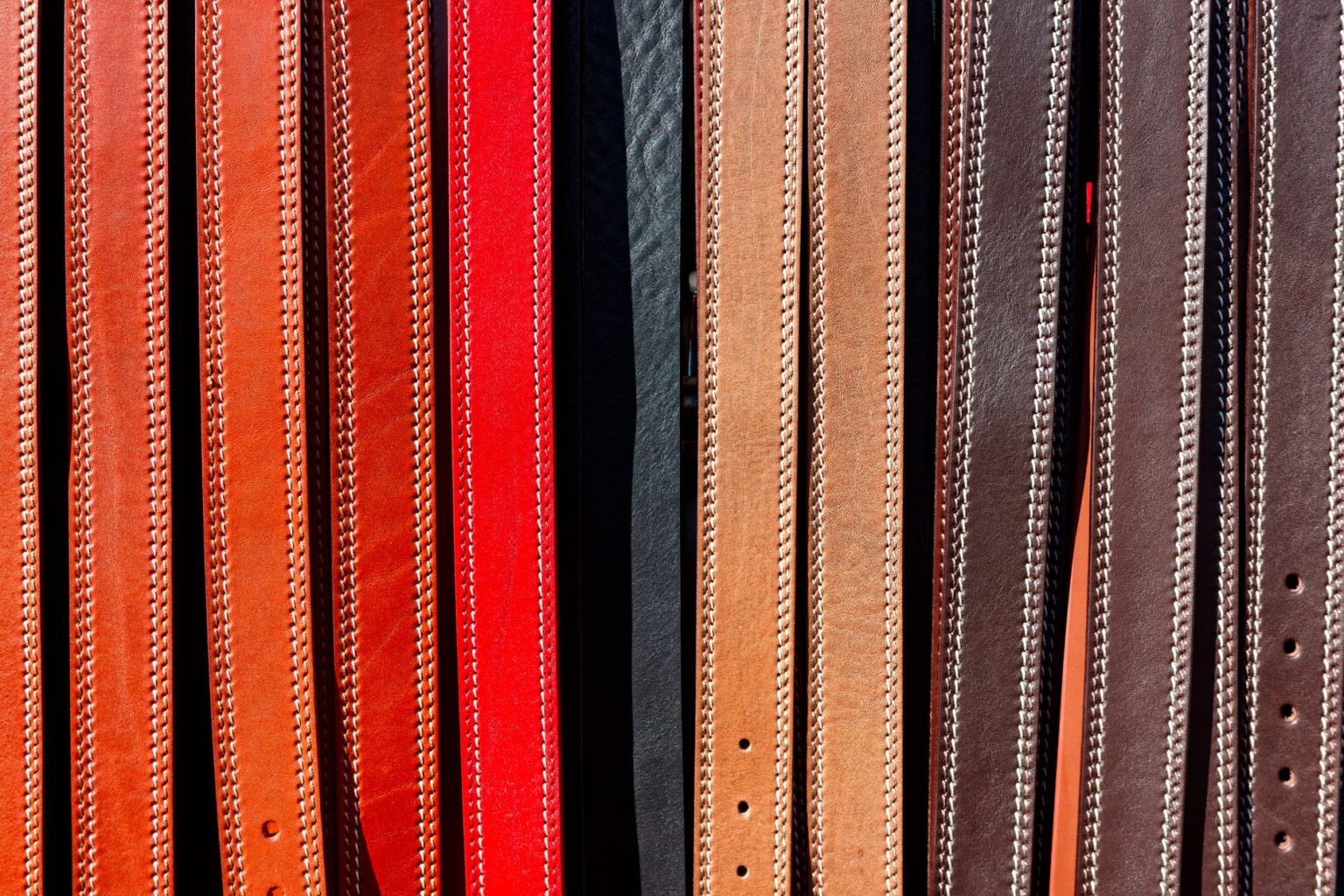 A narrow cognac leather belt with simple brass buckle laid flat on a neutral surface